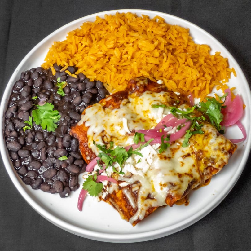 A plate of cheesy enchiladas with red sauce, black beans, and orange rice.