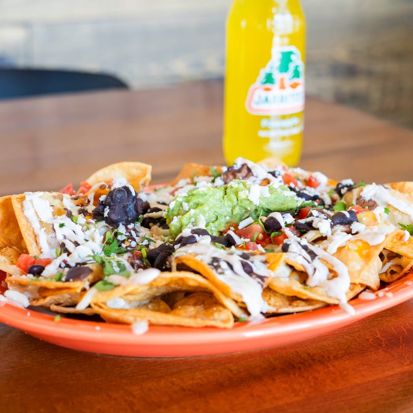Loaded nachos with guacamole, black beans, cheese, and sour cream, with a Jarritos bottle.